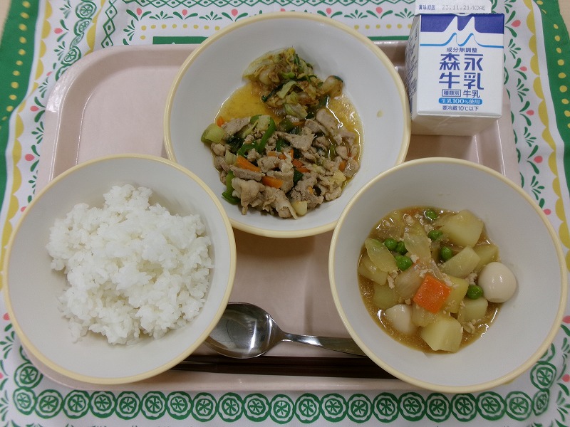 ピンクのトレーに給食が右上から反時計回りで牛乳、豚肉と長ねぎの炒め物と白菜の梅おかか和え、ご飯、じゃがいものそぼろ煮と並んでいる写真