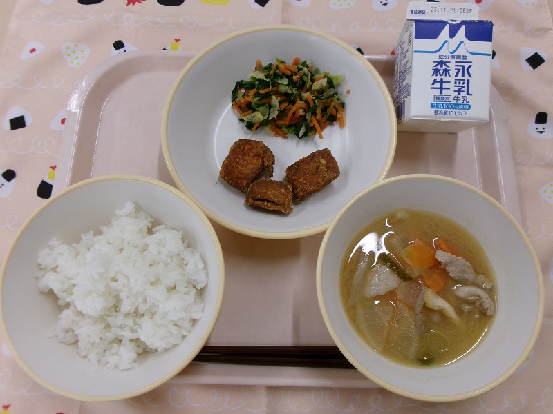 ピンクのトレーに給食が右上から反時計回りで牛乳、まぐろのピリ辛揚げと野菜のごま和え、ご飯、豚汁と並んでいる写真