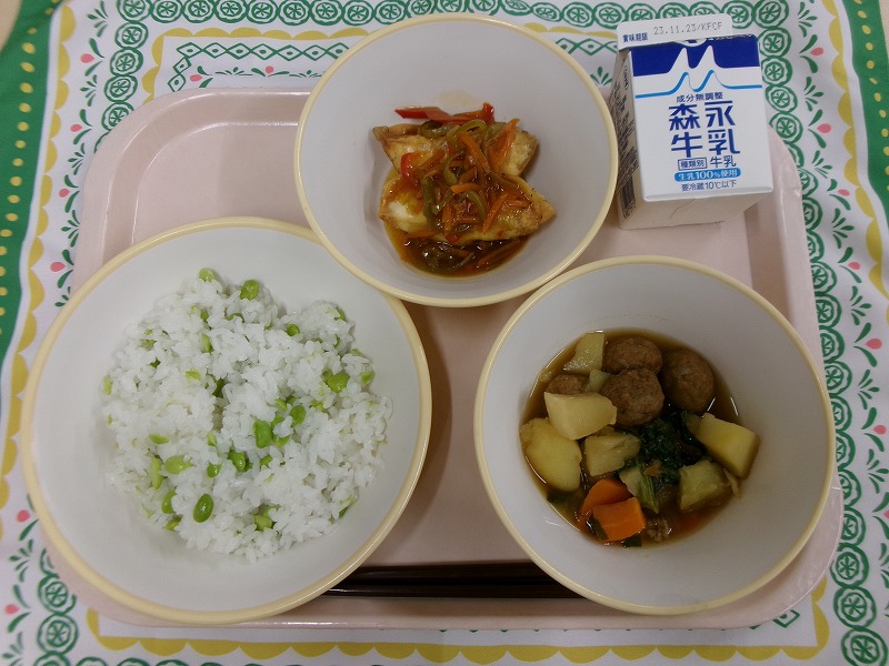 ピンクのトレーに給食が右上から反時計回りで牛乳、揚げ餃子の野菜あんかけ、枝豆ごはん、根菜と肉だんごの煮物と並んでいる写真