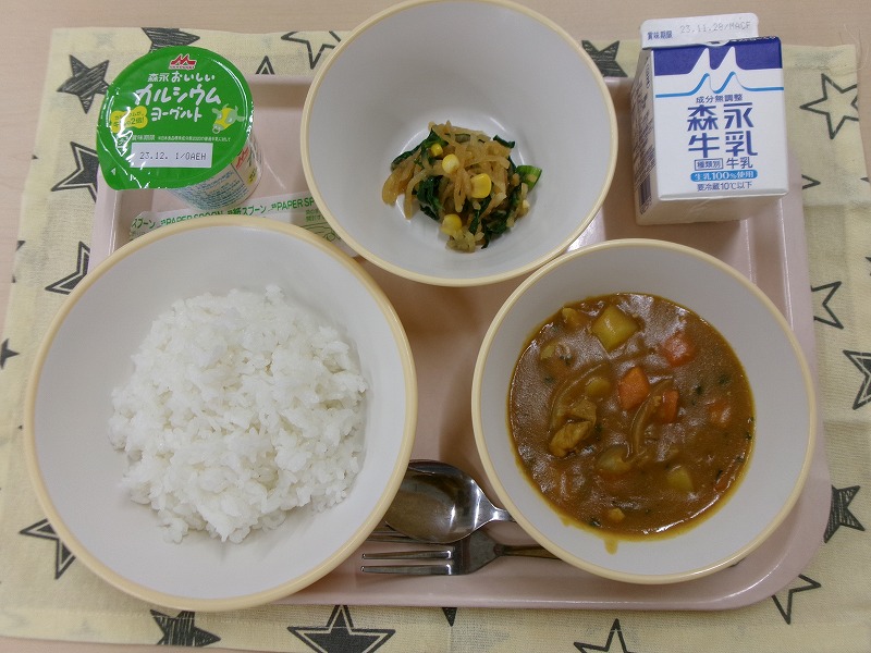ピンクのトレーに給食が右上から反時計回りで牛乳、大根サラダ、ヨーグルト、ご飯、チキンカレーと並んでいる写真