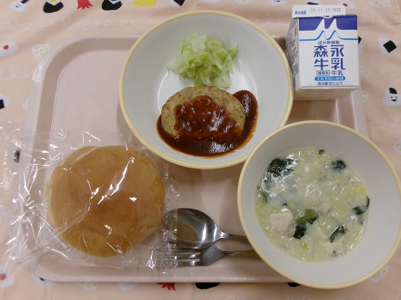 ピンクのトレーに給食が右上から反時計回りで牛乳、ハンバーグとサラダ、パン、白菜のクリーム煮と並んでいる写真