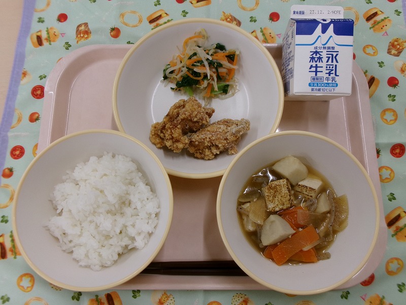 ピンクのトレーに給食が右上から反時計回りで牛乳、鶏の竜田揚げとナムル、ご飯、里芋と焼き豆腐の旨煮と並んでいる写真