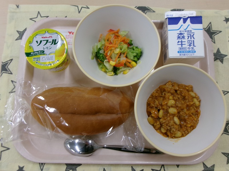 ピンクのトレーに給食が右上から反時計回りで牛乳、カラフルサラダ、レモンヨーグルト、コッペパン、チリコンカンと並んでいる写真
