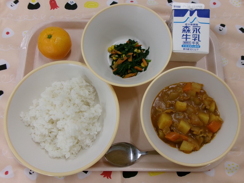 ピンクのトレーに給食が右上から反時計回りで牛乳、ほうれん草ソテー、みかん、ご飯、カレーと並んでいる写真