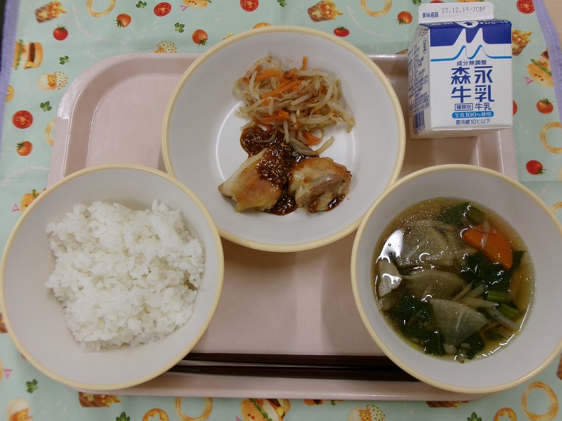 ピンクのトレーに給食が右上から反時計回りで牛乳、鶏肉のごま味噌焼きともやしのおかか和え、ご飯、みそけんちん汁と並んでいる写真