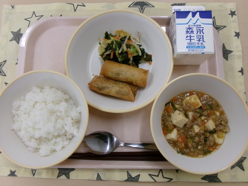 ピンクのトレーに給食が右上から反時計回りで牛乳、春巻きと海藻サラダ、ご飯、麻婆豆腐と並んでいる写真