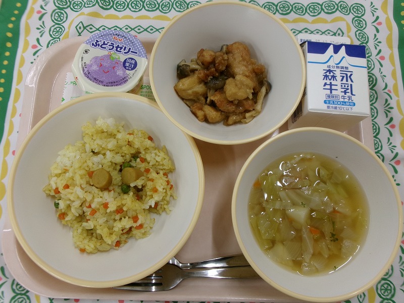 ピンクのトレーに給食が右上から反時計回りで牛乳、鶏肉のガーリック炒め、ぶどうゼリー、カレーピラフ、コンソメスープと並んでいる写真