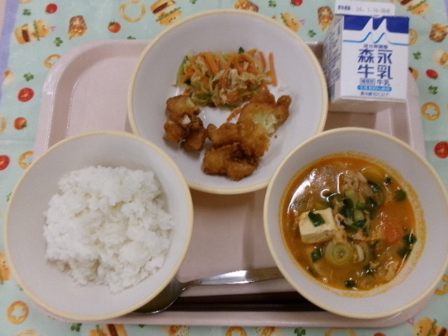 ピンクのトレーに給食が右上から反時計回りで牛乳、あげいもと韓国風サラダ、ご飯、キムチチゲと並んでいる写真