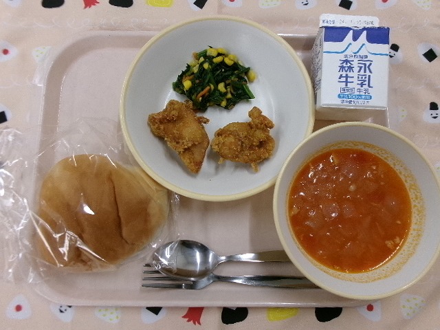 ピンクのトレーに給食が右上から反時計回りで牛乳、鶏のカレー揚げ、ほうれんそうソテー、ロールパン、ミネストローネと並んでいる写真