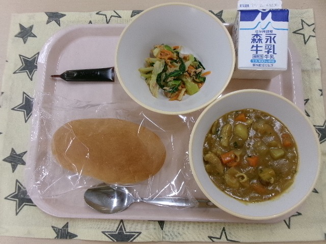 ピンクのトレーに給食が右上から反時計回りで牛乳、小松菜とツナのサラダ、ミルメーク、コッペパン、カレーシチューと並んでいる写真