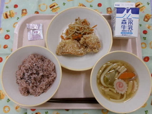 ピンクのトレーに給食が右上から反時計回りで牛乳、鶏のから揚げともやしのおかか和え、赤飯、きつねうどん汁と並んでいる写真