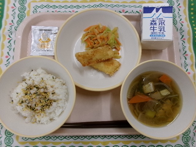 ピンクのトレーに給食が右上から反時計回りで牛乳、いかの吉野揚げとヤーコンのごまみそ和え、たまごふりかけ、ご飯、根菜汁と並んでいる写真