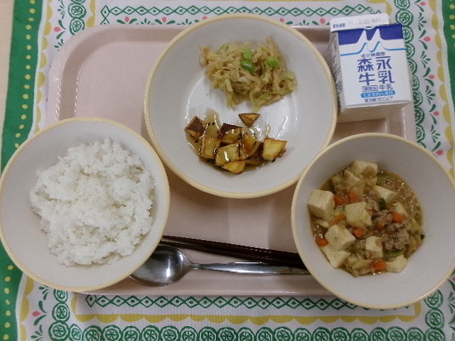 ピンクのトレーに給食が右上から反時計回りで牛乳、ささみと切り干し大根のサラダと大学芋、ご飯、麻婆豆腐と並んでいる写真