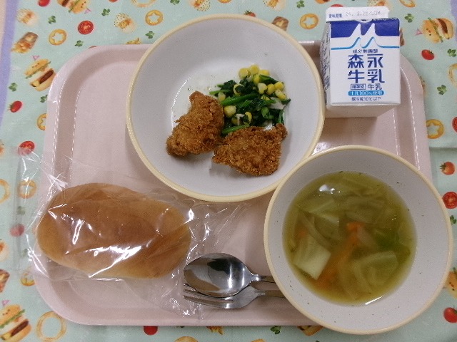 ピンクのトレーに給食が右上から反時計回りで牛乳、クリスピーチキンとポパイサラダ、ソフトフランスパン、コンソメスープと並んでいる写真