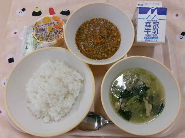 ピンクのトレーに給食が右上から反時計回りで牛乳、根菜入りキーマカレー、フルーツ野菜ゼリー、ご飯、キャベツのスープと並んでいる写真