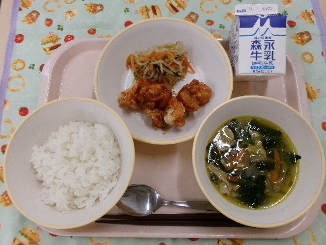 ピンクのトレーに給食が右上から反時計回りで牛乳、ヤンニョムチキンとナムル、ご飯、わかめスープと並んでいる写真