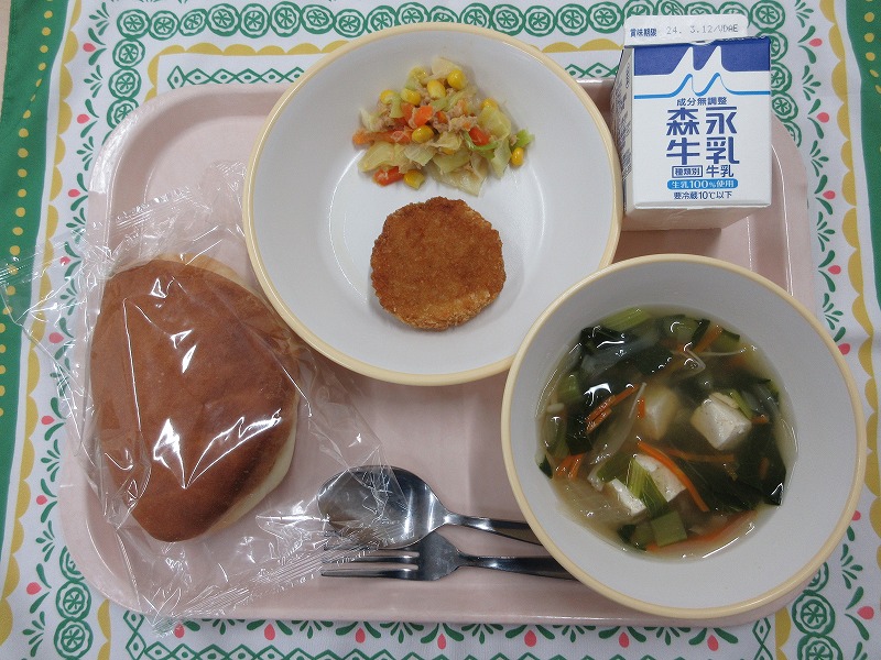 ピンクのトレーに給食が右上から反時計回りで牛乳、メンチカツと野菜のツナ炒め、パン、豆腐スープと並んでいる写真