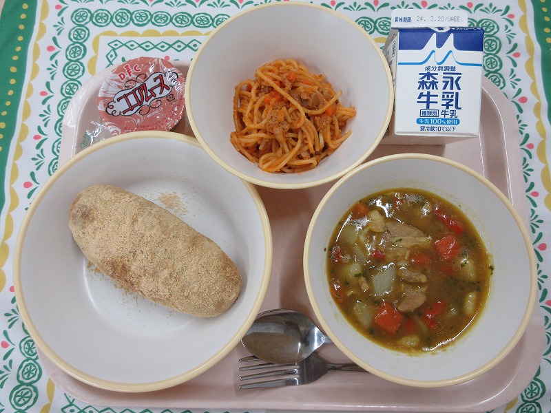 ピンクのトレーに給食が右上から反時計回りで牛乳、スパゲティミートソース、ココアムース、きな粉揚げパン、具だくさんスープカレーと並んでいる写真