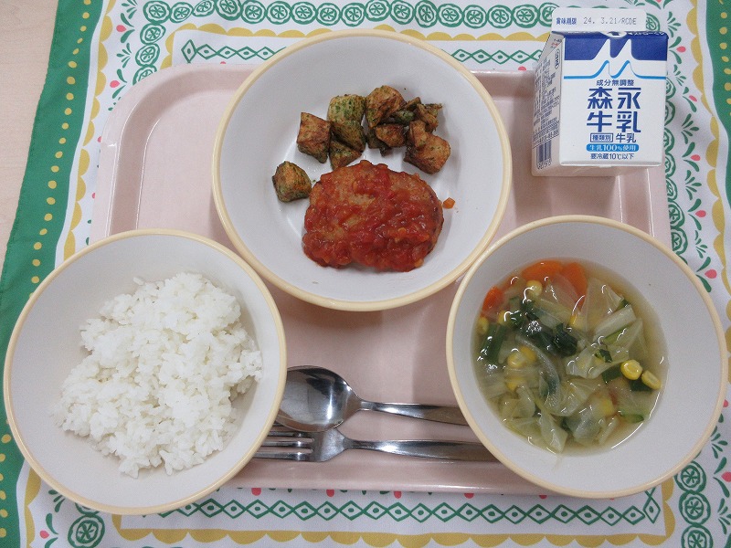 ピンクのトレーに給食が右上から反時計回りで牛乳、ハンバーグトマトソースと青のりポテト、ご飯、野菜スープと並んでいる写真