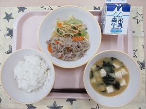 ピンクのトレーに給食が右上から反時計回りで牛乳、豚肉のピリ辛炒めと玉ねぎドレッシングサラダ、ご飯、わかめの味噌汁と並んでいる写真
