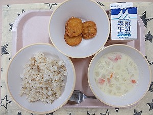 ピンクのトレーに給食が右上から反時計回りで牛乳、チキンナゲット、ガーリックライス、コーンのミルクスープと並んでいる写真