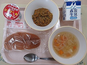 ピンクのトレーに給食が右上から反時計回りで牛乳、ドライカレー、ヨーグルト、パン、コンソメスープと並んでいる写真