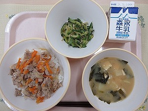 ピンクのトレーに給食が右上から反時計回りで牛乳、ピリ辛きゅうり、豚丼（もち麦入りごはん）、じゃがいもの味噌汁と並んでいる写真
