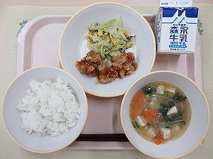 ピンクのトレーに給食が右上から反時計回りで牛乳、鶏肉のかりん揚げとごまドレッシングサラダ、ご飯、五目スープ並んでいる写真