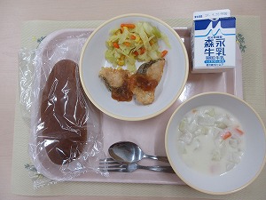 ピンクのトレーに給食が右上から反時計回りで牛乳、白身魚のバーベキューソースとキャベツソテー、黒パン、かぶのミルクスープと並んでいる写真