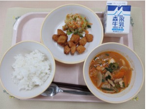 ピンクのトレーに給食が右上から反時計回りで牛乳、韓国風サラダ、あげいも、ご飯、キムチチゲと並んでいる写真