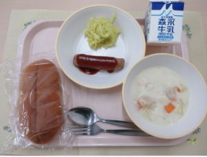 ピンクのトレーに給食が右上から反時計回りで牛乳、ウインナーソーセージとキャベツ、パン、ほたてのクリームシチューと並んでいる写真