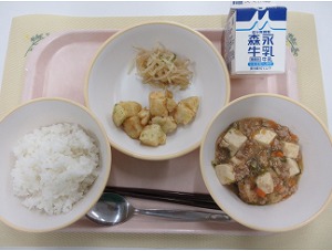 ピンクのトレーに給食が右上から反時計回りで牛乳、もやしナムルと青のりポテト、ご飯、麻婆豆腐と並んでいる写真