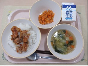 ピンクのトレーに給食が右上から反時計回りで牛乳、にんじんしりしり、甘辛からあげ丼、野菜スープと並んでいる写真