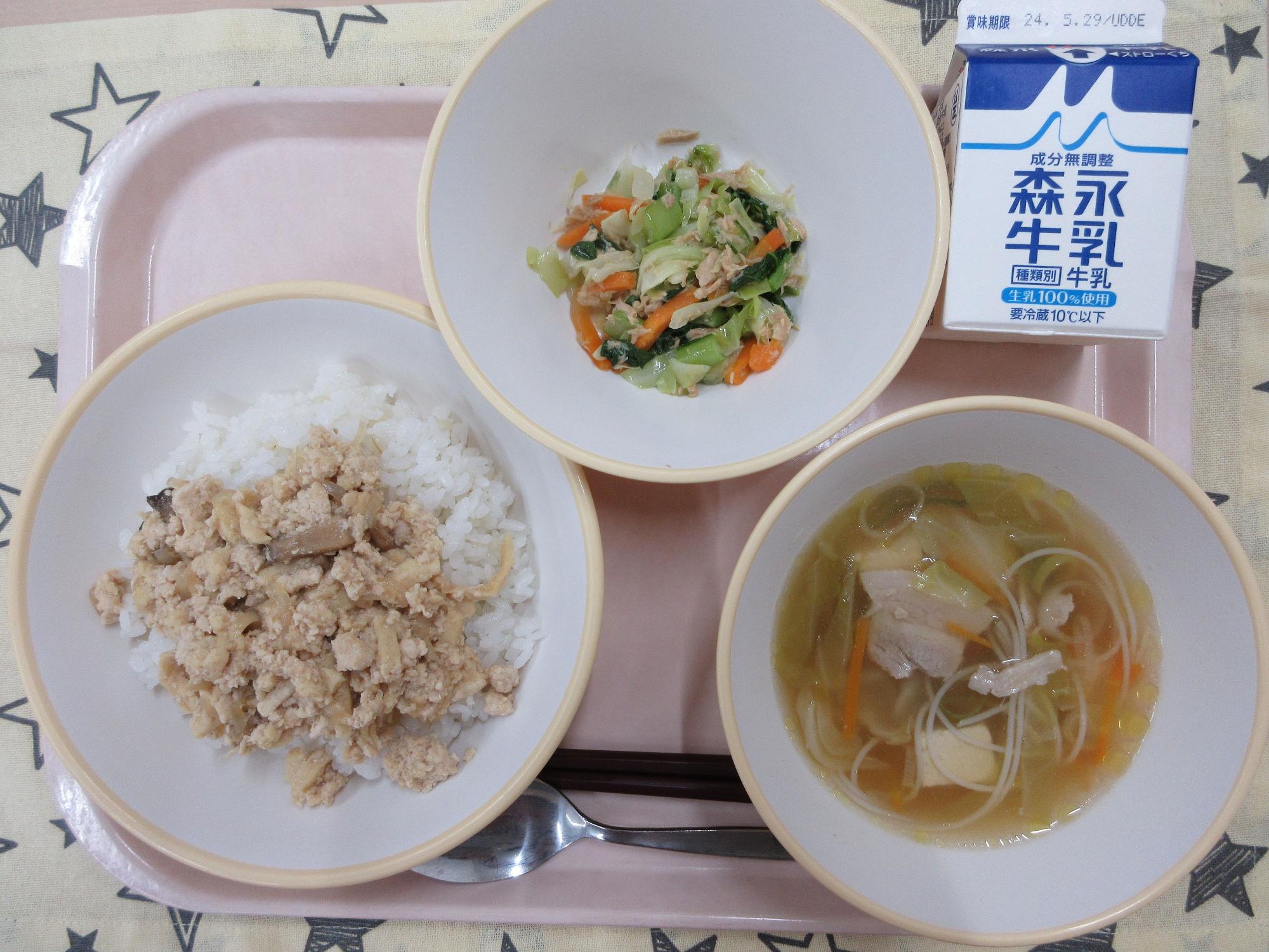 ピンクのトレーに給食が右上から反時計回りで牛乳、野菜のツナ炒め、鶏そぼろ丼、ビーフンスープと並んでいる写真
