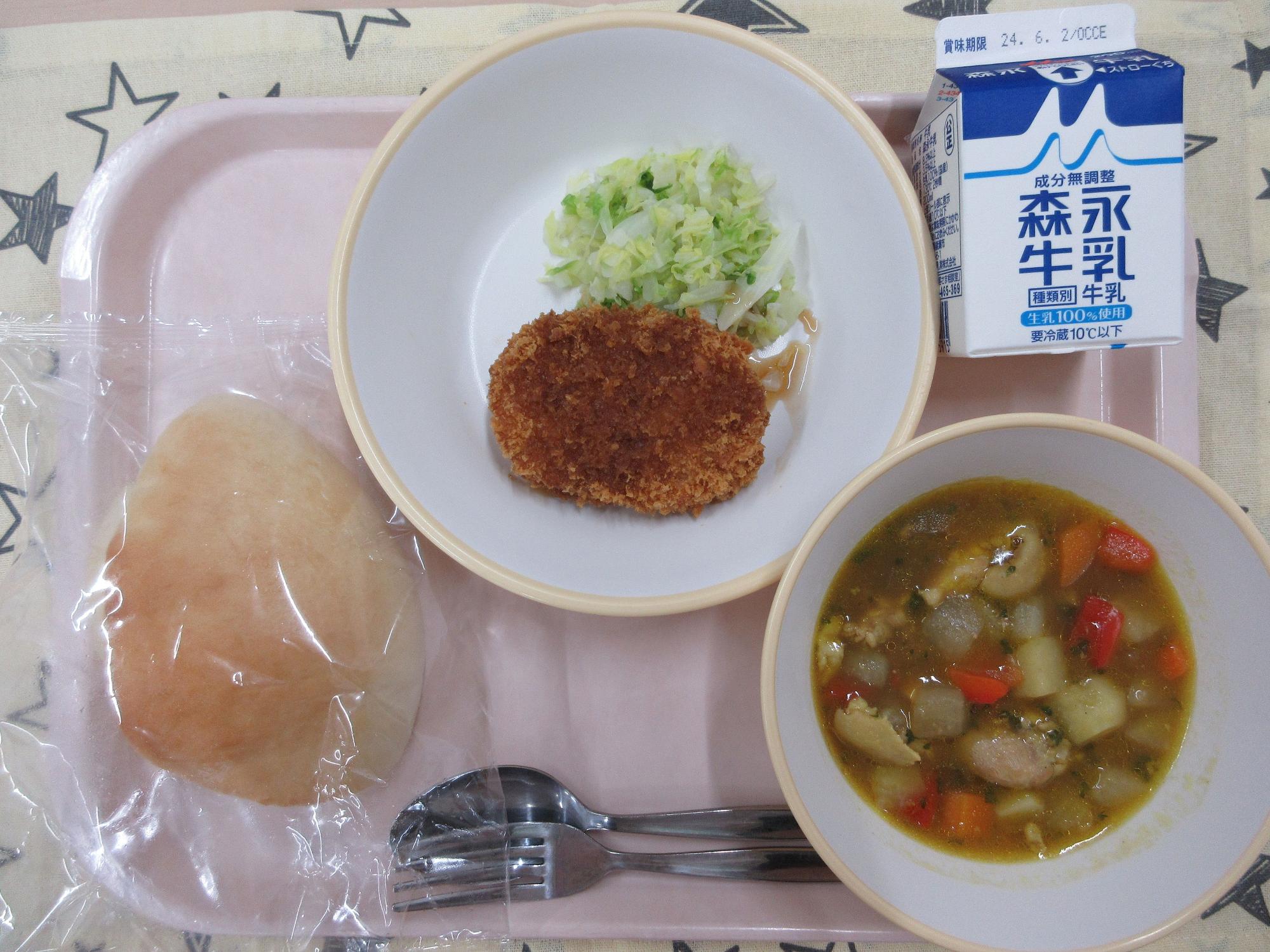 ピンクのトレーに給食が右上から反時計回りで牛乳、コロッケとキャベツ、パン、具だくさんスープカレーと並んでいる写真