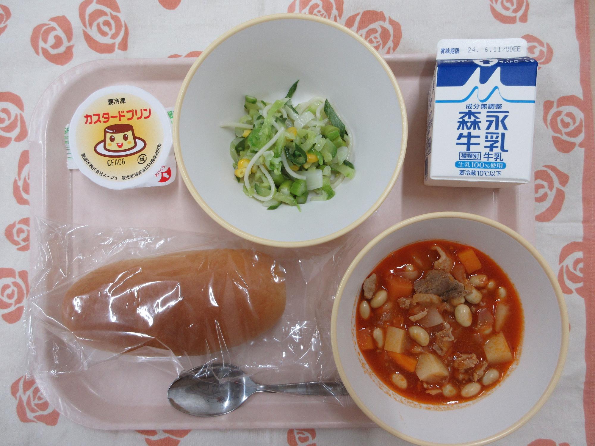 ピンクのトレーに給食が右上から反時計回りで牛乳、グリーンサラダ、カスタードプリン、ソフトフランスパン、ポークビーンズと並んでいる写真