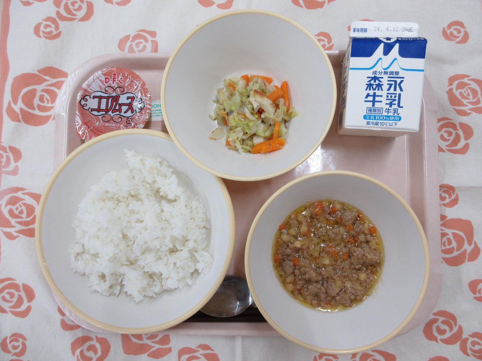 ピンクのトレーに給食が右上から反時計回りで牛乳、野菜のごま炒め、ココアムース、もち麦入りごはん、肉みそと並んでいる写真