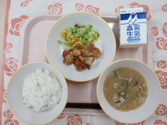 ピンクのトレーに給食が右上から反時計回りで牛乳、鶏肉の香味ソースがけとコールスローサラダ、ご飯、豚汁と並んでいる写