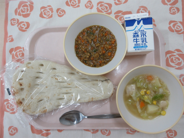 ピンクのトレーに給食が右上から反時計回りで牛乳、キーマカレー、ナン、野菜のスープ煮と並んでいる写真