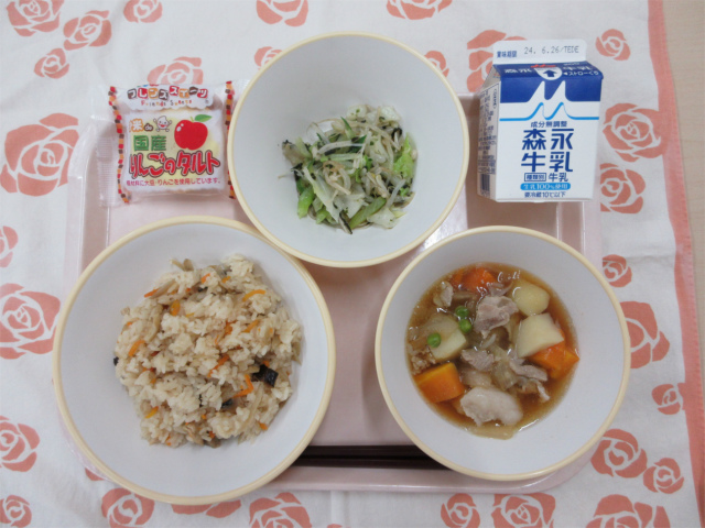 ピンクのトレーに給食が右上から反時計回りで牛乳、磯香和え、りんごタルト、かやくごはん、肉じゃがと並んでいる写真