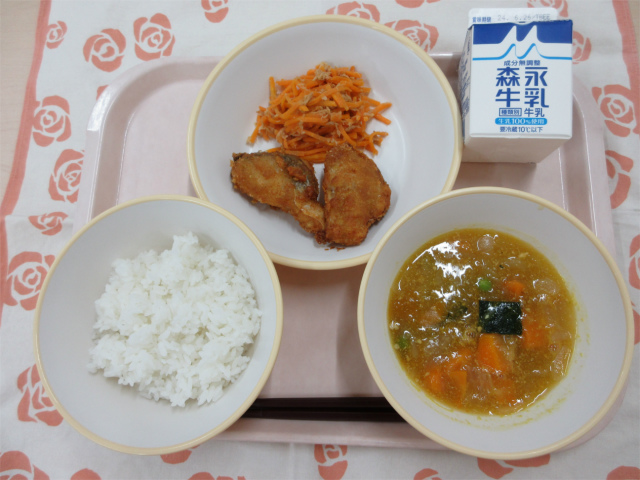 ピンクのトレーに給食が右上から反時計回りで牛乳、白身魚のカレー揚げとにんじんしりしり、ご飯、かぼちゃのそぼろ煮と並んでいる写真