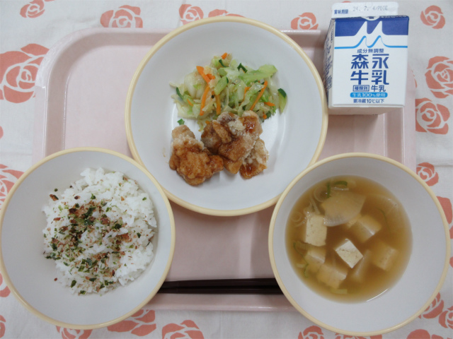 ピンクのトレーに給食が右上から反時計回りで牛乳、鶏肉の甘酢だれとうま塩キャベツ、おかかふりかけのご飯、、すまし汁と並んでいる写真