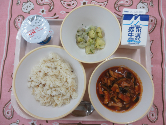 ピンクのトレーに給食が右上から反時計回りで牛乳、ジャーマンポテト、ヨーグル、ガーリックライス、ラタトゥイユと並んでいる写真