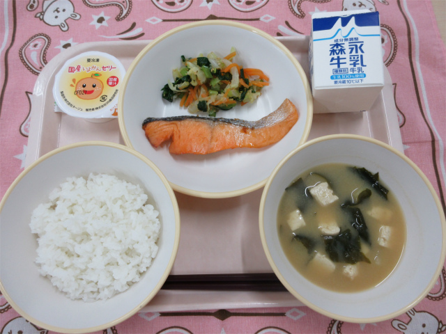ピンクのトレーに給食が右上から反時計回りで牛乳、鮭の塩焼きとごま和え、いよかんゼリー、ご飯、わかめの味噌汁と並んでいる写真