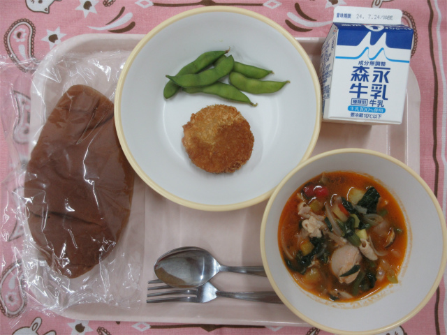 ピンクのトレーに給食が右上から反時計回りで牛乳、メンチカツと枝豆、黒パン、チキンカチャトーラと並んでいる写真