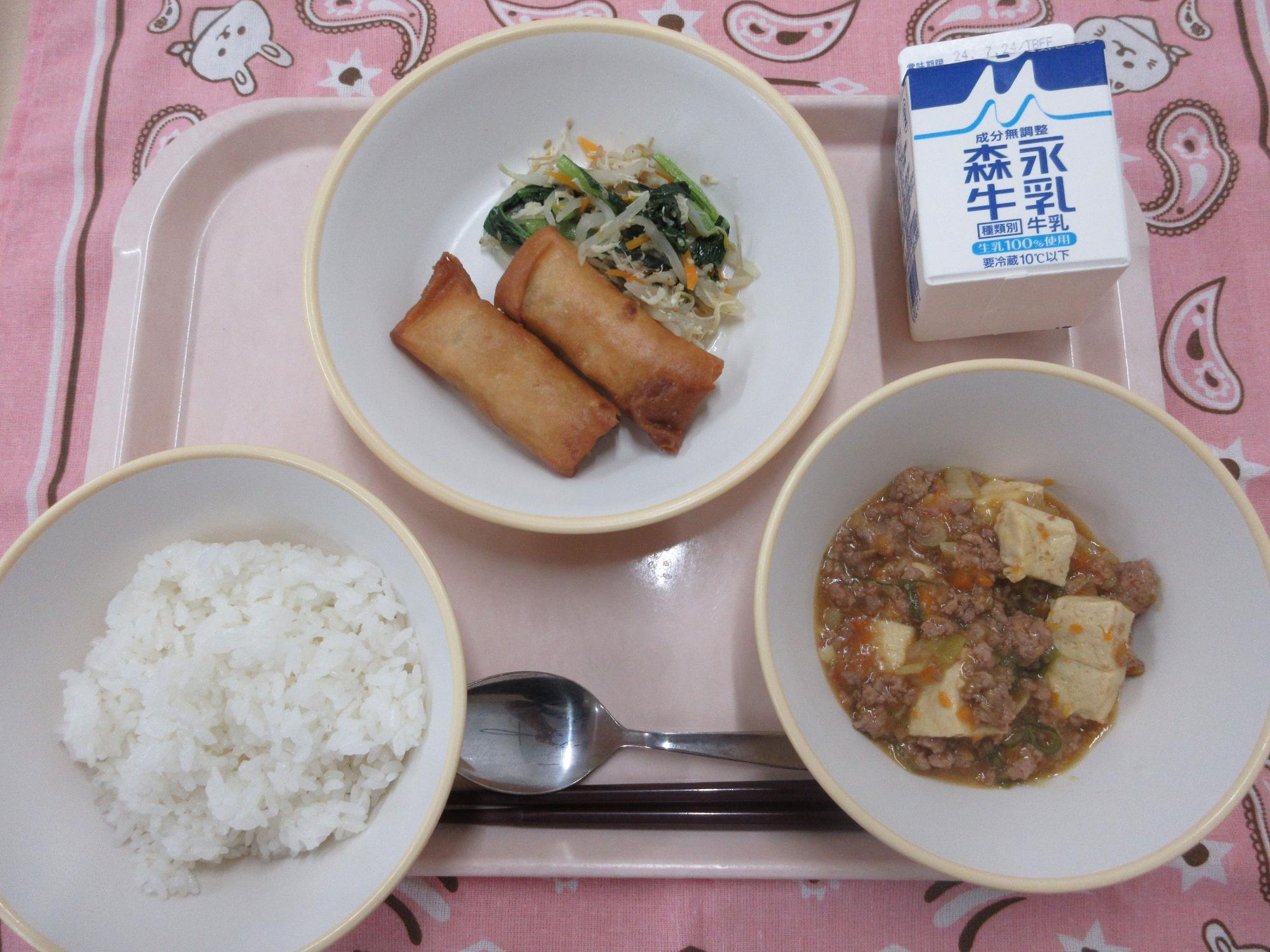 ピンクのトレーに給食が右上から反時計回りで牛乳、春巻きと鶏ささみの中華炒め、ご飯、麻婆豆腐と並んでいる写真