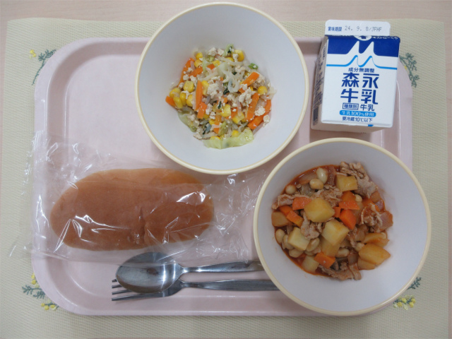 ピンクのトレーに給食が右上から反時計回りで牛乳、白滝ソテー 、ソフトフランスパン、ポークビーンズと並べられている写真