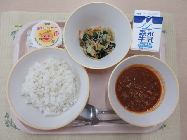 ピンクのトレーに給食が右上から反時計回りで牛乳、海藻サラダ 、いよかんゼリー、もち麦入りごはん、トマトとひき肉のアジアンライスのルーと並べられている写真