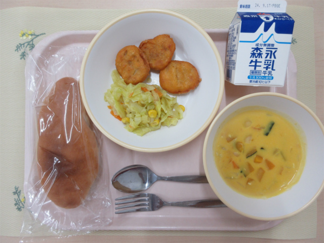 ピンクのトレーに給食が右上から反時計回りで牛乳、チキンナゲット、キャベツソテー、コッペパン、かぼちゃのクリームスープと並べられている写真