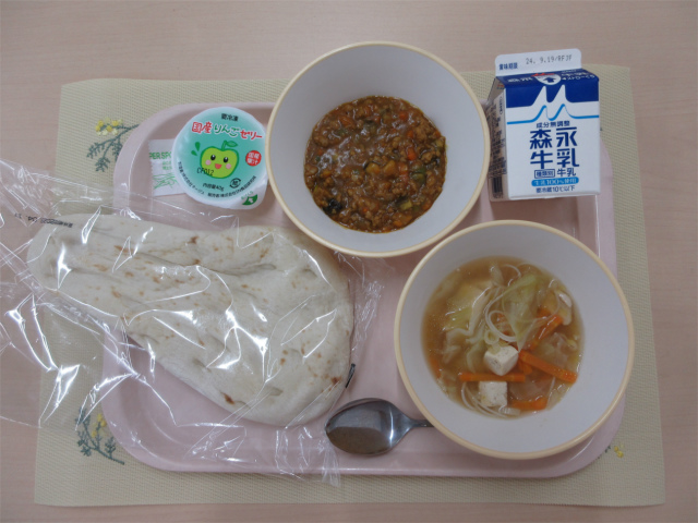 ピンクのトレーに給食が右上から反時計回りで牛乳、キーマカレー、りんごゼリー、ナン、ビーフンスープと並べられている写真